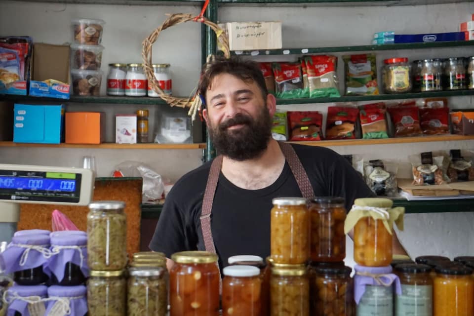 A shop owner standing behind a counter of jars and goods