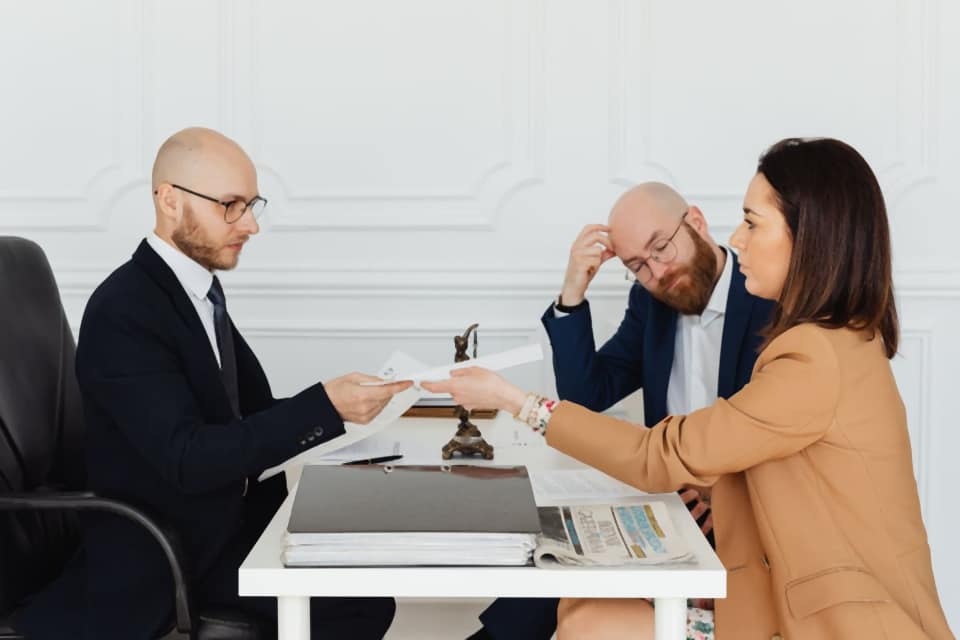 A client passing a sheet of paper to a lawyer at a white desk