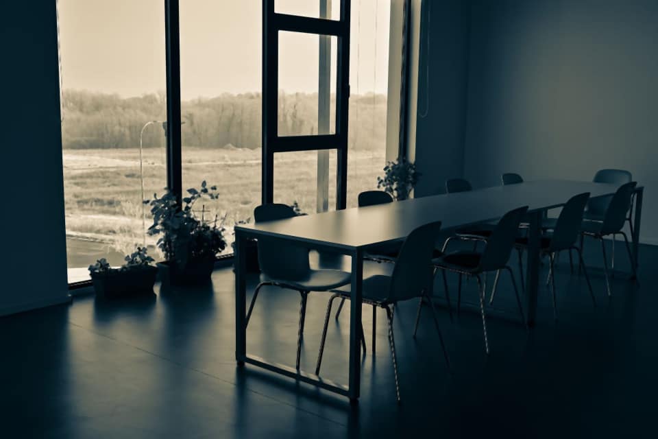 An empty meeting room with a long table and tall windows