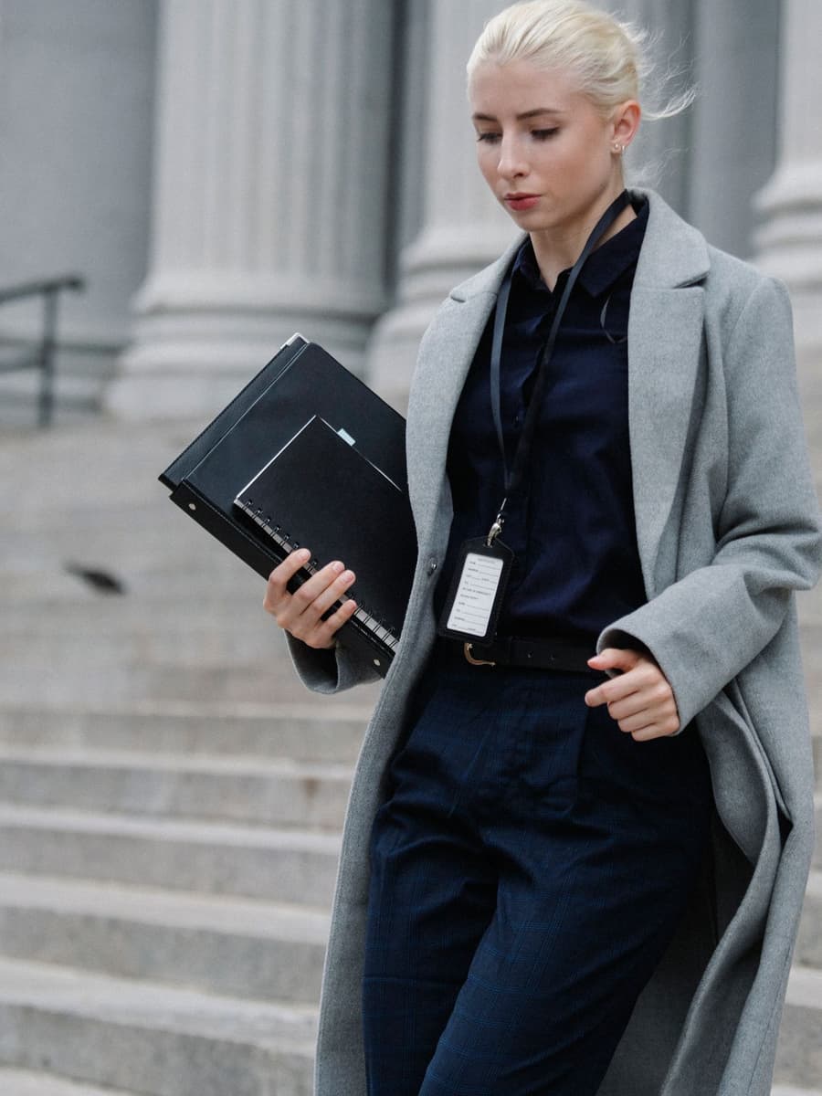 A woman in a grey coat carrying folders down the steps of a court building