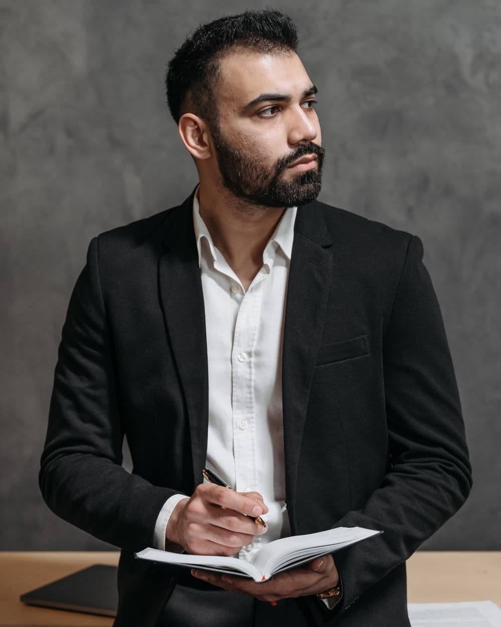 Taylor Sample leaning on a desk with a notebook and pen, looking to one side