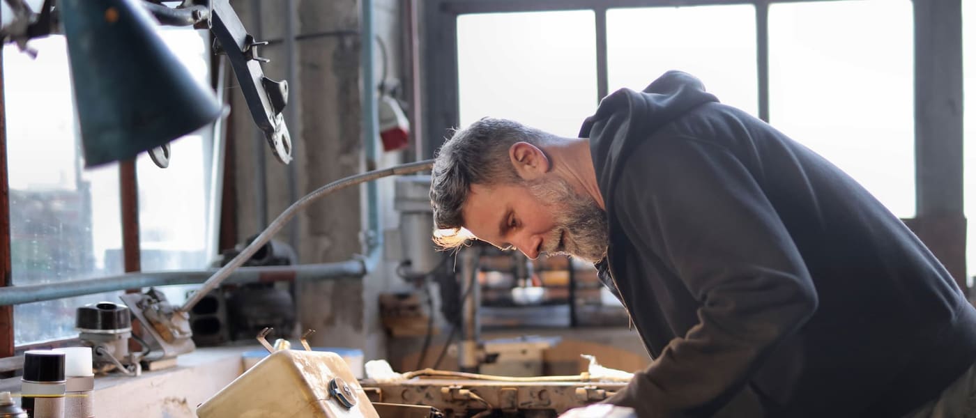 A woodworker leaning over a bench in a workshop full of tools