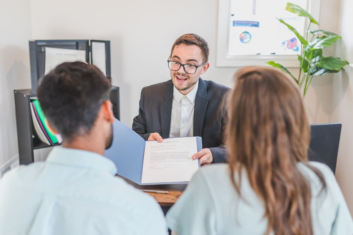 An accountant in glasses handing documents to a couple at a desk