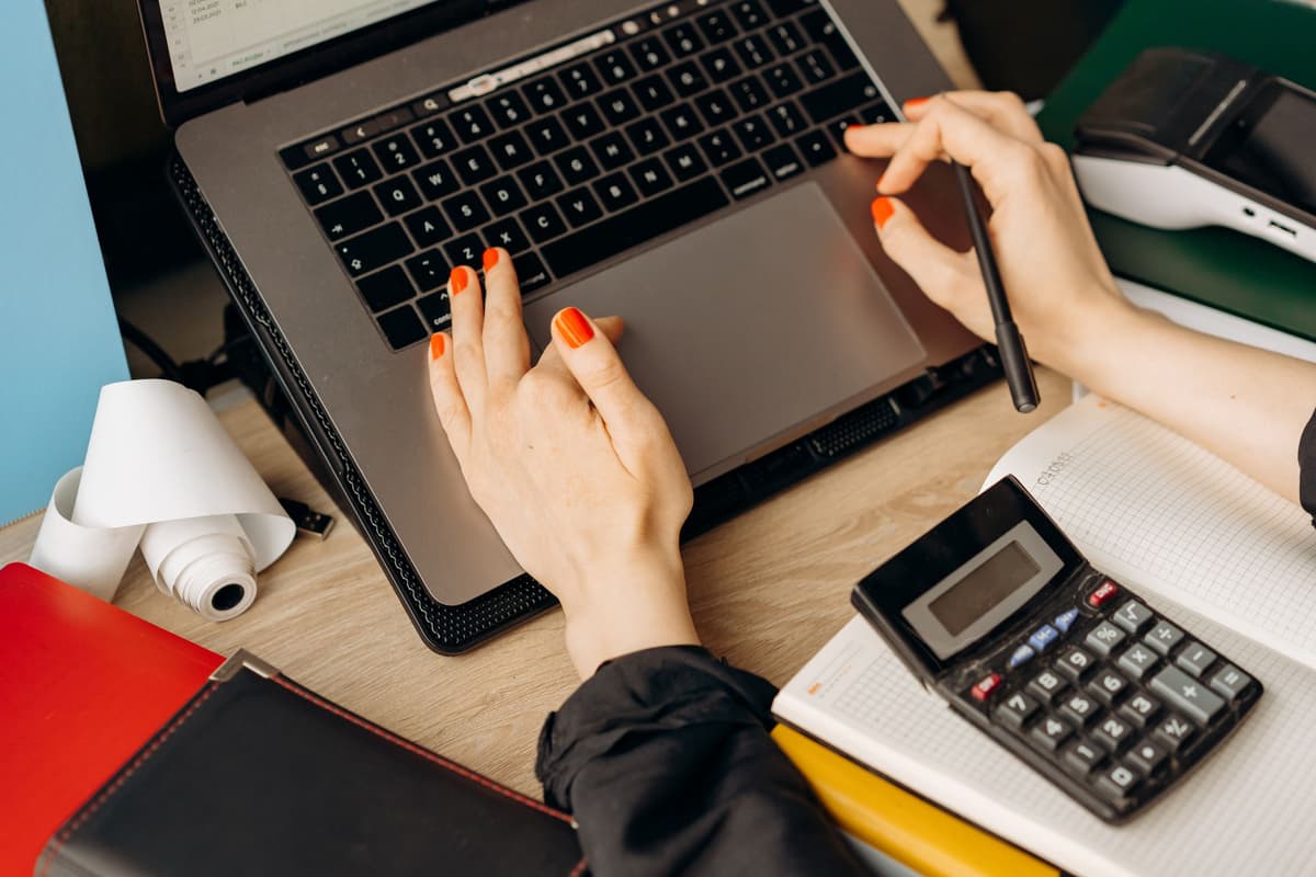 Hands on a laptop trackpad next to a calculator and a stack of folders