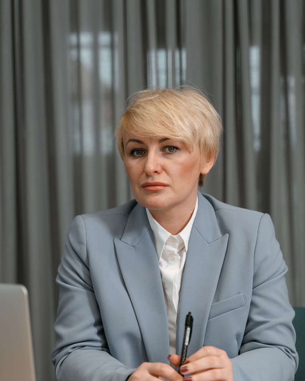 Ashley Sample in a grey blazer at a desk with a pen