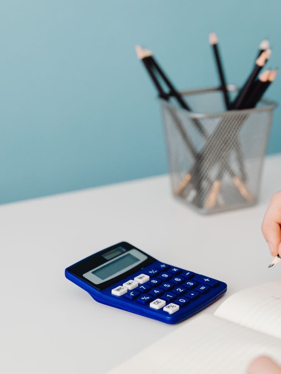A blue calculator and a cup of pencils on a pale desk