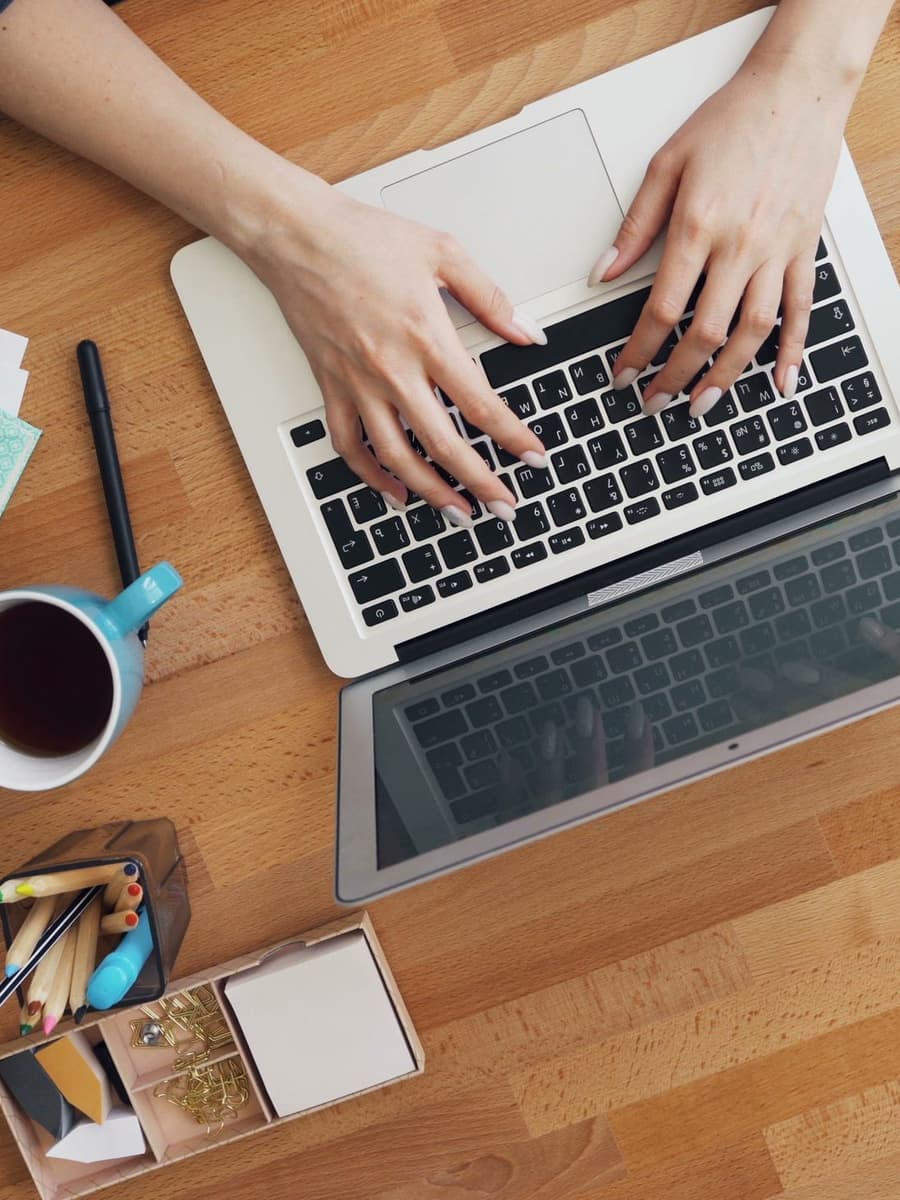 Hands typing on a laptop on a wooden desk, seen from above